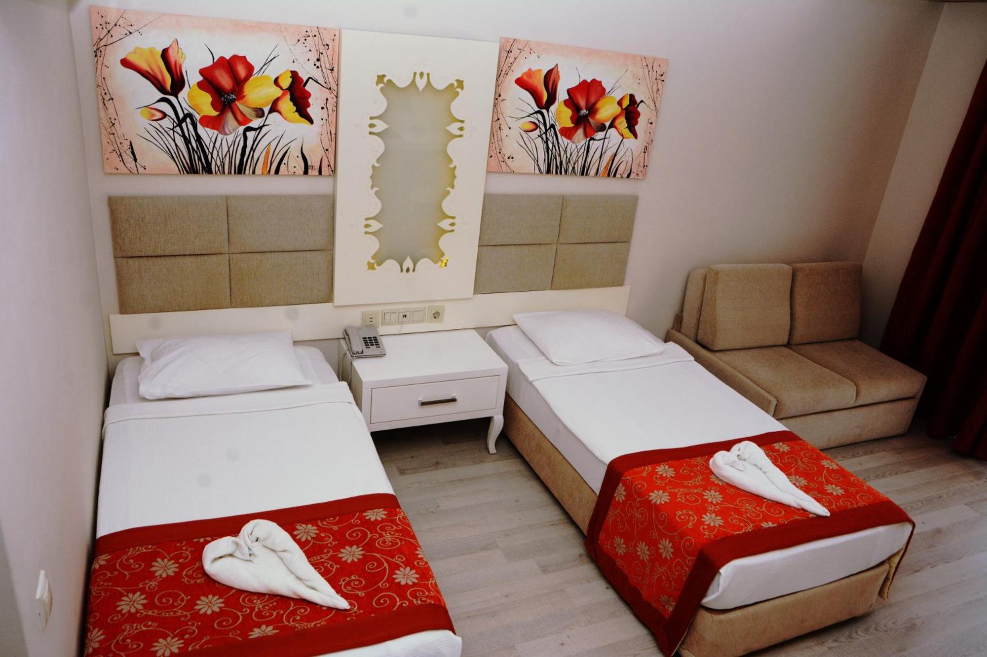 Miramor Hotel & Spa Antalya Exterior photo The photo shows a hotel room featuring two single beds with white linens, each adorned with a decorative red throw. The headboards are upholstered in a light beige fabric. Above the beds, there are two large artwork pieces depicting colorful flowers.